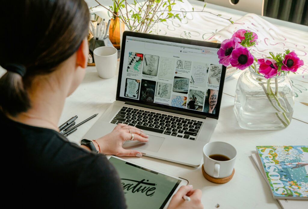 girl working on laptop on table with cup of coffee and book with pencil and flower flask